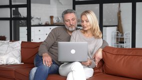 Carefree middle-aged spouses using laptop sitting on the sofa in modern living room, happy grey-haired husband hugging wife, romantic mature couple with laptop at home shopping online, making order - Powered by Shutterstock - Get 15% off with code: PIKWIZARD15