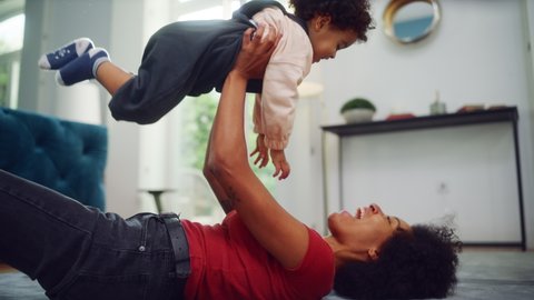 Beautiful Multiethnic Mother Playing with Adorable Baby Boy at Home on Living Room Floor. Cheerful Mom Nurturing a Child. Happy Son Raised in the Air. Concept of Childhood, New Life, Parenthood.