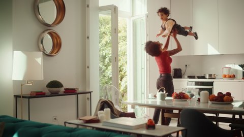 Happy Mother Holding Adorable Baby Boy, Playing, Having Fun at Modern Home Living Room. Black Female Lifting Up and Throwing Toddler Child Up in the Air. Concept of Childhood, New Life, Parenthood.