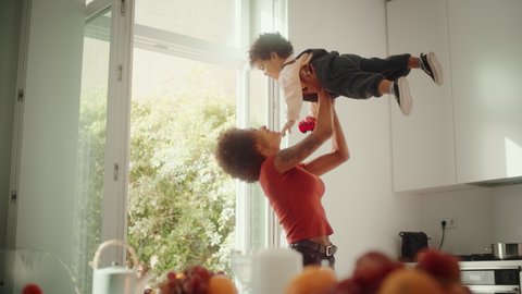 Happy Mother Holding Adorable Baby Boy, Playing, Having Fun at Modern Home Living Room. Latina Female Lifting Up and Throwing Toddler Child Up in the Air. Concept of Childhood, New Life, Parenthood.