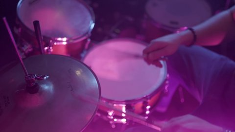 Young musician faceless drummer playing drums with drumsticks at concert party in night club. Close up. Man drumming with sticks performing live at stage colorful light hands back side view.