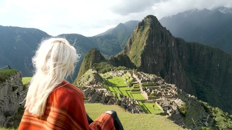 4K View of Machu Picchu. Beautiful blonde girl looking at Machu Picchu. Machu Picchu, the lost city of the Andes, located above the Sacred Valley of Cuzco, Urubamba, Peru. Famous view of Machu Picchu.