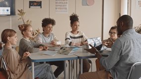 Medium slowmo of cheerful multiethnic schoolchildren and their African-American teacher sitting in circle at desk in bright modern Science class talking to each other and laughing - Powered by Shutterstock - Get 15% off with code: PIKWIZARD15