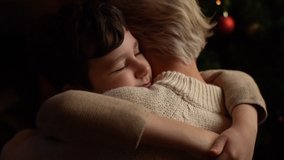Close-up back view of happy little child son hugging loving young mother near Christmas tree decorated balls and glowing garland in dark living room, in Christmas eve, enjoying holiday together - Powered by Shutterstock - Get 15% off with code: PIKWIZARD15