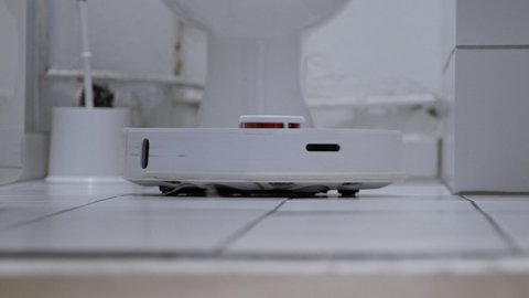 Low Angle of Robotic Vacuum Cleaner moving into close up on white tiles in a bathroom.