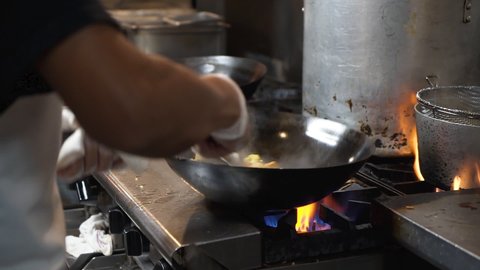 Chef flips and tosses fried rice in wok over flaming fire on commercial stovetop in restaurant kitchen, slowmotion HD