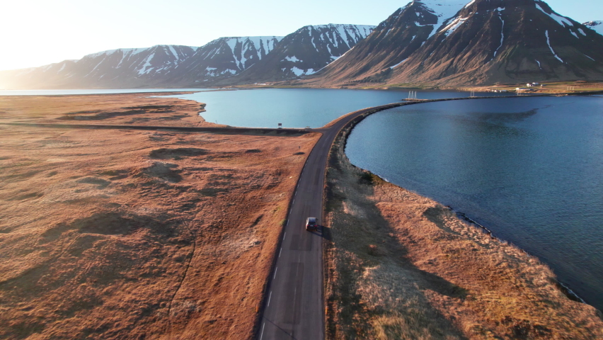 Wide Drone Shot Tracking Car Driving Along Empty Road Over Fjords Towards Sunlit Mountain Range, Isafjordur, Westfjords, Iceland | Shutterstock HD Video #1083326278
