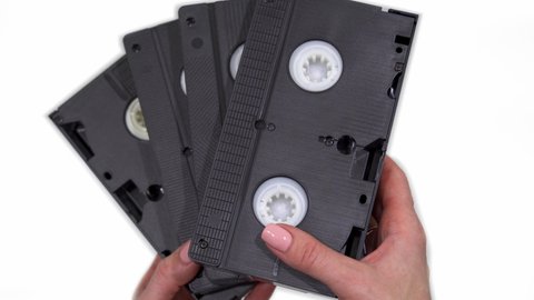 Old analog videotapes in the hands of a woman, on a white background.