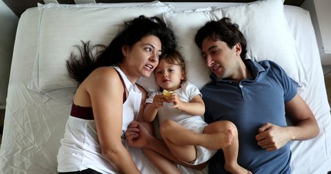 Joyful parents with baby infant in bed interaction, happy loving millennial family. Top view