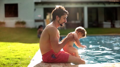 Father holding toddler baby at outdoor swimming pool