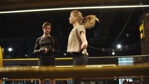 Serious coach counting jumps on boxing ring. Closeup sporty girl exercising with jump rope in sport club. Energetic sport woman jumping on skipping rope at gym.