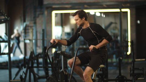 Closeup eager male athlete doing cardio in fitness center. Sporty fitness man training on exercycle at gym. Active sport man using velosimulator in sport club.