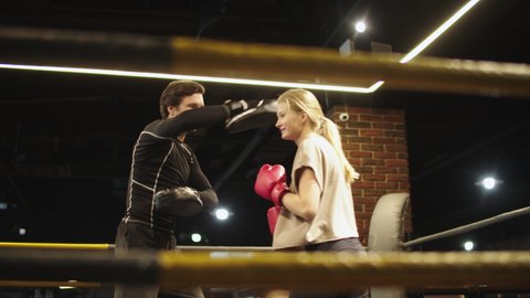 Smiling sport woman doing punches on boxing ring. Male boxer giving instructions at gym. Beautiful fit girl training with coach in sport club.