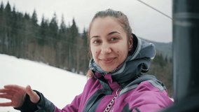 Happy woman making video calls to friends on mobile phone at ski resort in mountains, selfie in winter mountains, tourist blogger records live broadcast