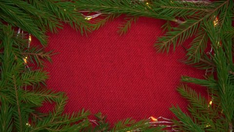 Background for Christmas. Red cloth surrounded by spruce branches and garlands. A hand puts a box with a gift in the center. Silver shiny gift box, Happy New Year and Merry Christmas greetings concept