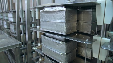 Numerous stainless steel containers for butter. Steel reticulated boxes for butter stored on the tall metal shelves. Modern dairy enterprise.