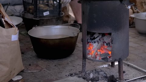 Street Chef Prepares Potatoes on a Wood Stove with Glowing Coals. Man sorts potatoes with hands and puts them in a box. Cooking of grilled vegetables with steam and smoke. Zoom. Slow motion.