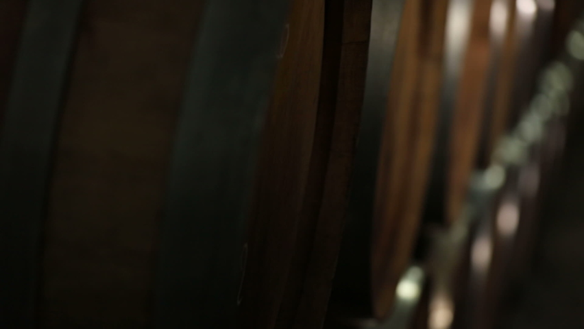 A Wine Cellar. Storage Room for Wine in Bottles and Barrels. Old wine in a dark underground vault. Wooden oak whiskey, wine, cognac, brandy or beer barrels. Bottles on wooden shelves.