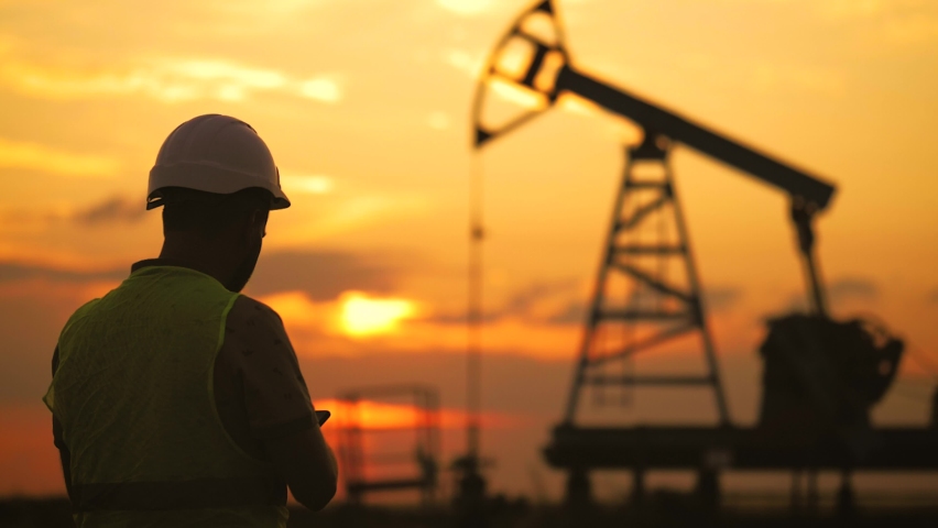 Silhouette working engineer oil rig. Oil rigs at sunset. Silhouette of man engineer with phone overseeing the site of crude oil production at sunset. Industrial, oil and gas concept. Royalty-Free Stock Footage #1083348484