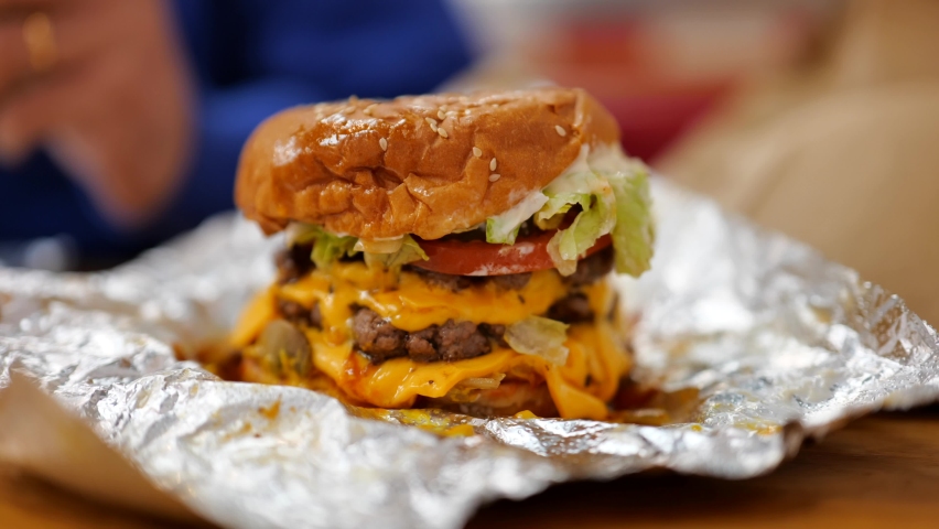 Triple patty beef burger with cheese, lettuce and tomato on foil wrapper