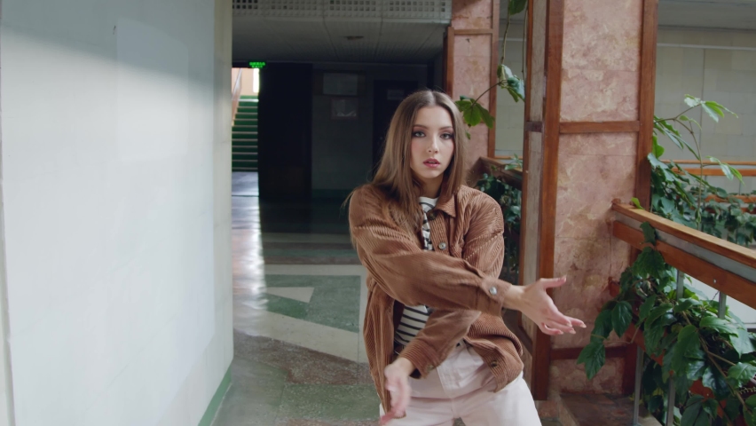 Young woman, confident choreographer is dancing in hallway, decorated with green plants, looking and walking on camera, full of energy and inspiration, Slow motion.