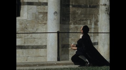 1800s: Man sits at base of the Leaning Tower of Pisa and makes notes with quill pen. Man stands up and watches balls fall to ground. Two balls on the ground.