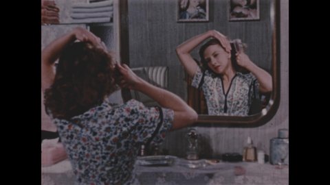 1950s: Woman ties hair back with small comb. Woman combs and styles hair in mirror at vanity. Woman spins and shows off hairdo.