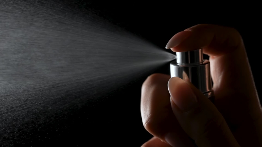 Woman's hand finger sprays perfume on black background. Small particles of eau de toilette scatter in space. Cologne spray isolated in the dark with backlight. Close up. Slow motion. | Shutterstock HD Video #1083362407