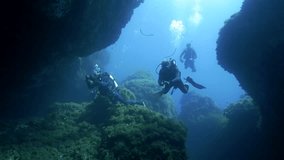 underwater shot of scuba divers entering a huge underwater cave in mediterranean sea, wide shot, ustica island, italy