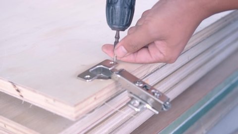 Hand of a craftsman using screws to install cabinet hinges on wooden cabinet doors. with skill
