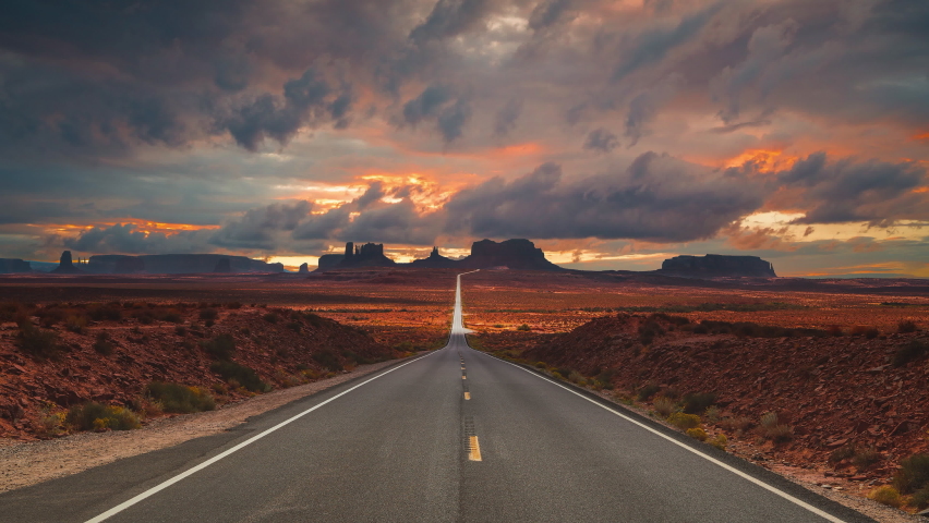 Scenic and cinematic golden red cloud sunset time-lapse at the iconic Forrest Gump spot road at the Monument Valley tea kettle rocks landmarks in Utah, Arizona, America USA. Cinemagraph seamless video Royalty-Free Stock Footage #1083369517