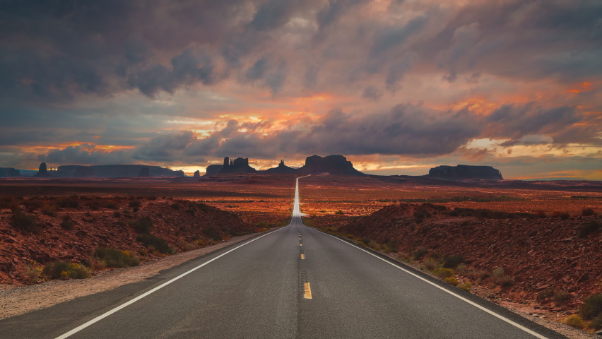 Scenic and cinematic golden red cloud sunset time-lapse at the iconic Forrest Gump spot road at the Monument Valley tea kettle rocks landmarks in Utah, Arizona, America USA. Cinemagraph seamless video | Shutterstock HD Video #1083369517