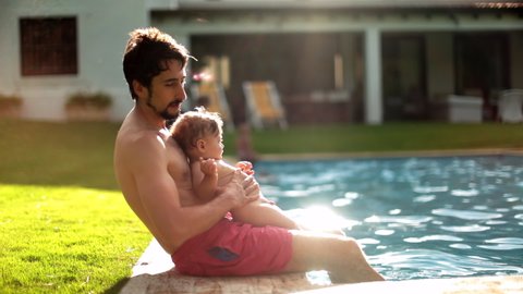 Father and baby boy son together at swimming pool outside in backyard