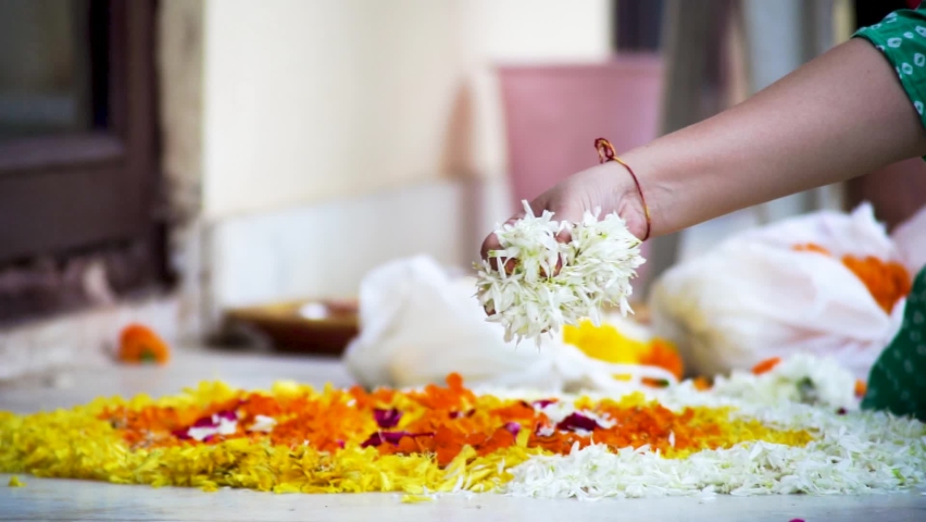 Slow motion shot of Indian woman dropping marigold jasmine flowers on a rangoli pattern on the floor while making a rangoli for diwali, new year or a wedding decoration as part of the hindu religion