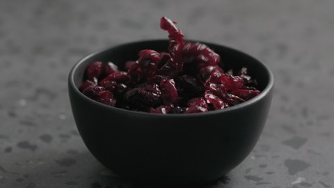 Slow motion dried cranberry falling into black bowl on terrazzo countertop