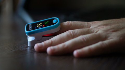 Pulse oximeter in a male patient's fingertip on dark wooden table background, medical equipment, portable oximeter, pneumonia prevention, covid-19 pandemic consequences