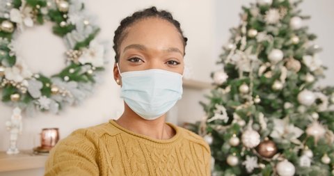 POV of happy African American woman in masks isolated at home with decorated christmas tree with lights video chatting online and greeting friends and relatives with xmas. Xmas eve in quarantine