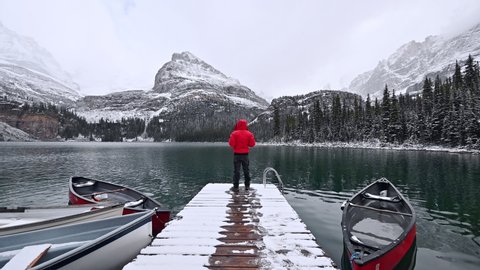 Traveler standing on wooden pier with rocky mountains in snowing at Lake O'hara, Yoho national park, Canada