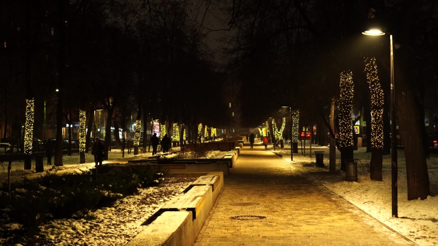 A woman walks down a street decorated with Christmas lanterns, lights on a winter evening in a snowfall, a snow storm