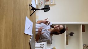 Young woman trainer coach shoot webinar speak by camera of smartphone at home office. Female student pass oral exam by video call answer teacher question before phone fixed on holder. Vertical video - Powered by Shutterstock - Get 15% off with code: PIKWIZARD15