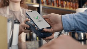 Pay by phone on pos terminal at coffee bar. E-money transfer from electronic wallet of client. Payment machine or card reader in barista hands close-up. Male buyer in cafeteria or food super market - Powered by Shutterstock - Get 15% off with code: PIKWIZARD15