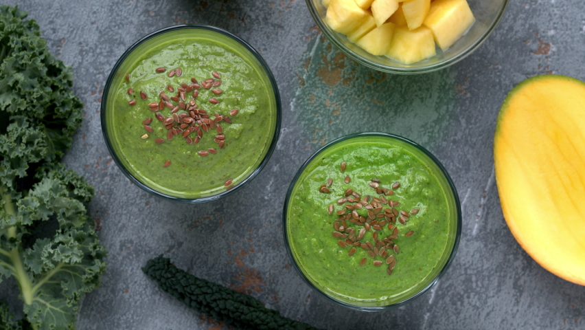 Green smoothie glasses with curly kale and lacinato kale leaves and ingredients. Top view of detox healthy breakfast. Table spin. | Shutterstock HD Video #1083400057