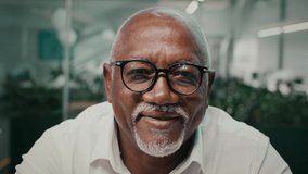 Closeup Portrait Of Happy Mature Black Businessman Wearing Eyeglasses Smiling At Camera, Cheerful Middle Aged African American Entrepreneur Posing In Modern Office Interior, Slow Motion Footage