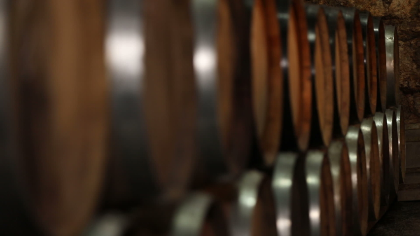A Wine Cellar. Storage Room for Wine in Bottles and Barrels. Old wine in a dark underground vault. Wooden oak whiskey, wine, cognac, brandy or beer barrels. Bottles on wooden shelves. Royalty-Free Stock Footage #1083402898