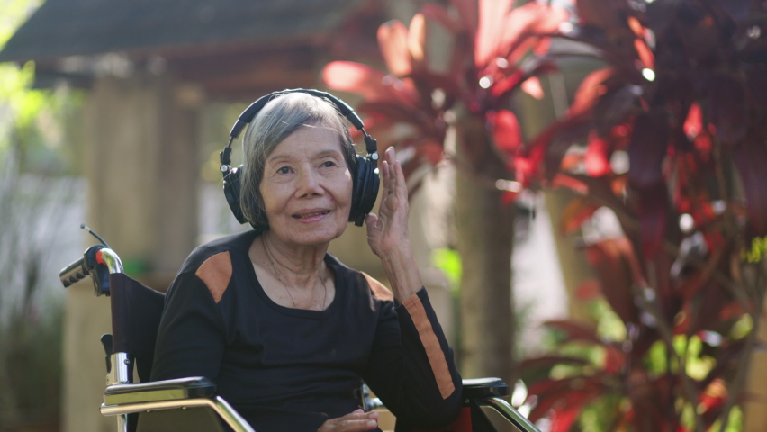 Asian senior woman listening music with headphone in backyard. Royalty-Free Stock Footage #1083403006