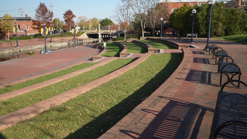Frederick, MD, USA - 11 11 2021: Day time autumn view of popular city park, Carroll Creek Park in historic district of Frederick with shops and building on sides of the canal. People walking.