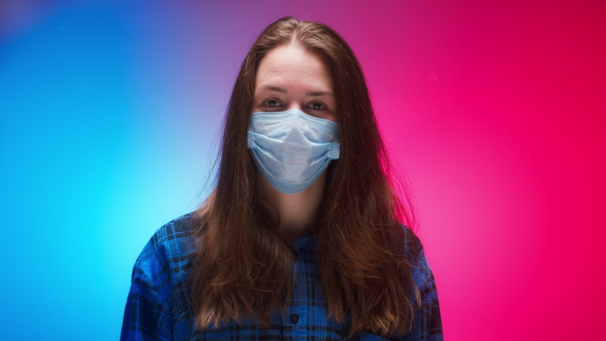Woman wearing medical mask showing on phone vaccination passport with qr code, international coronavirus covid 19 vaccine certificate on mobile device, green zone. Red and blue neon background. Royalty-Free Stock Footage #1083405883