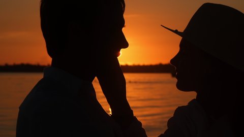 Young couple hug and kiss at sunset on the beach. A loving man and woman are hugging in the bright rays of the sun on the background of the ocean. Passionate guy and a girl in love