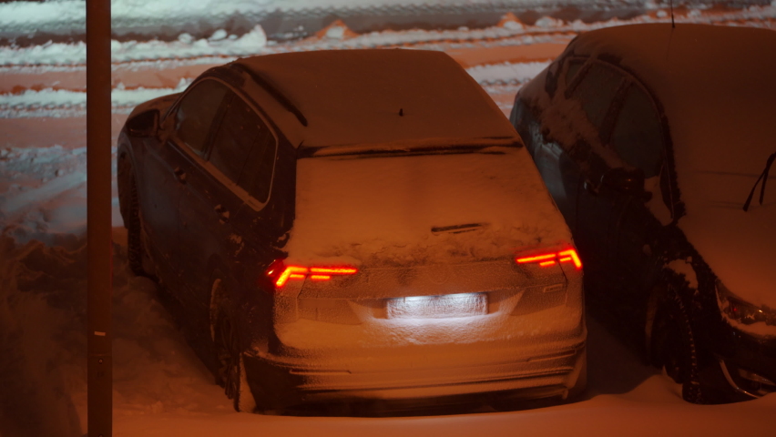 Parked cars covered with snow at dusk under a street lamp in parking lot in winter. Heavy snowfall on city streets. High quality 4k footage