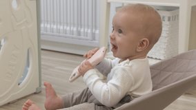 Cute toddler boy sitting on rocking chair in living room and watching something on mobile phone screen, 9 months old caucasian baby using smartphone at home. High quality 4k footage